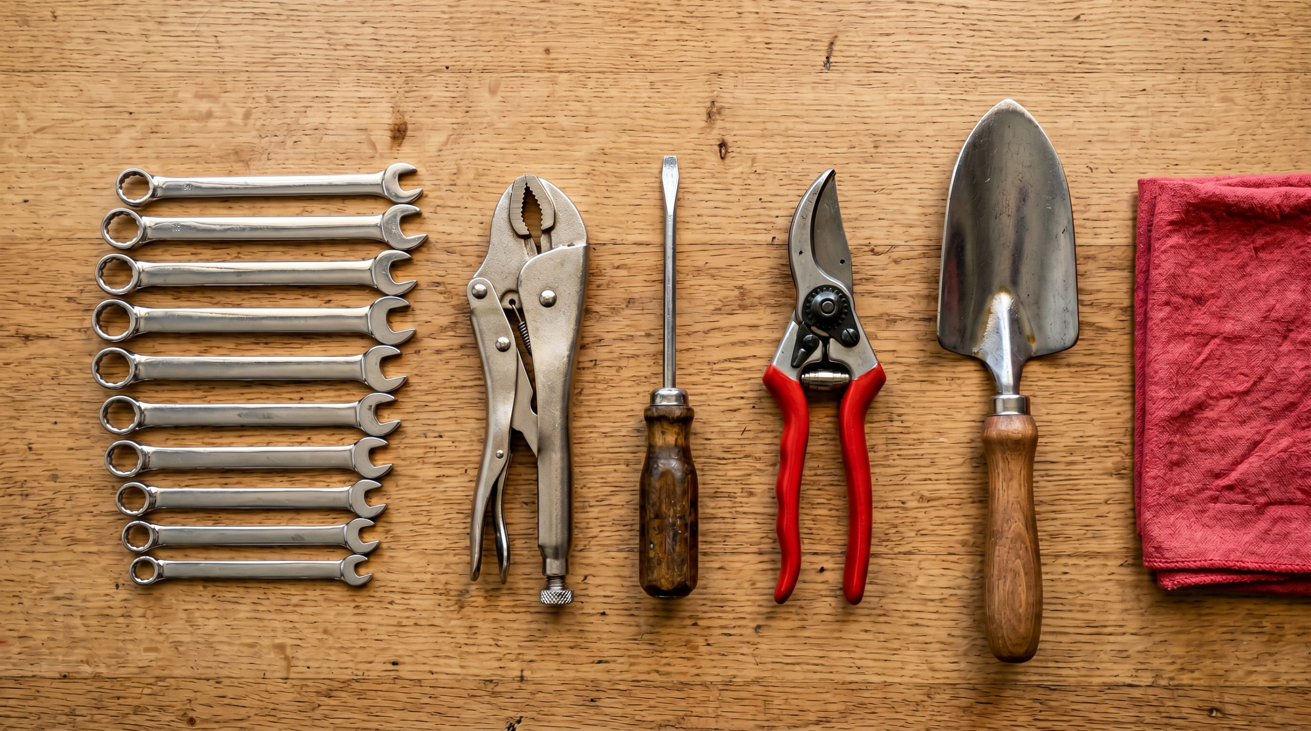Overhead flat lay of rust-free chrome wrenches pliers screwdriver pruning shears and hand trowel on a wooden workbench after protective oil treatment