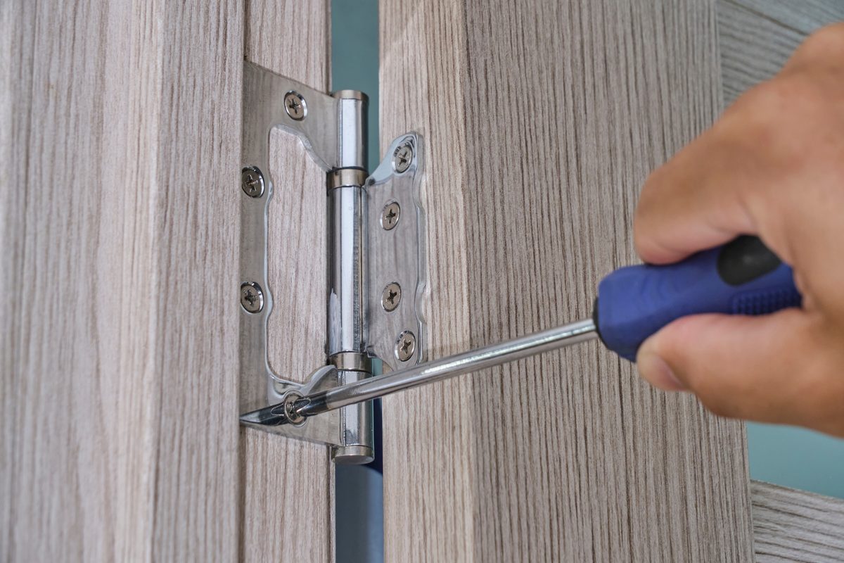 working on a door hinge with a screwdriver during the permanent squeak fix